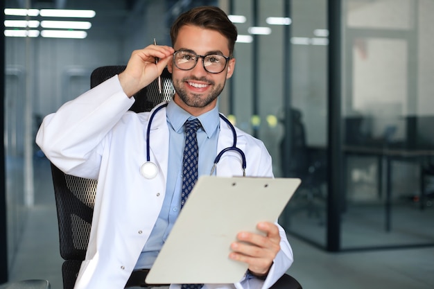 Beau jeune médecin sympathique dans le couloir de l'hôpital regardant la caméra, souriant.