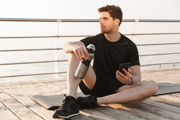 Beau jeune sportif assis à l'extérieur, écouter de la musique