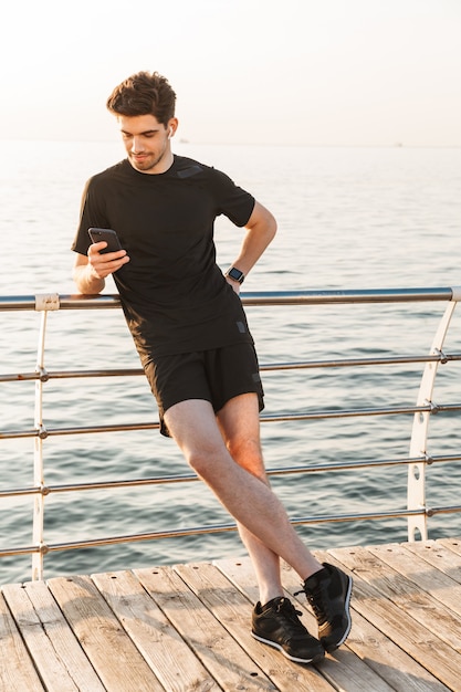 Beau jeune sportif écoute de la musique avec des écouteurs à l'aide de téléphone mobile.