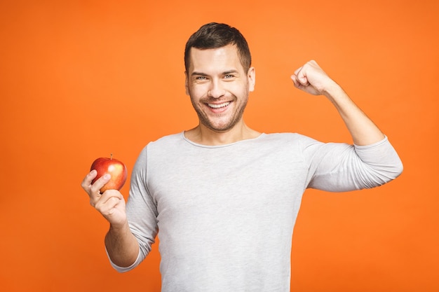 Beau jeune sportif montre ses muscles avec une pomme et souriant.