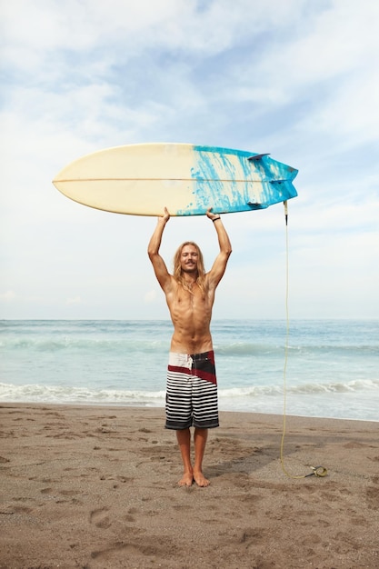 Beau jeune surfeur tenant une planche de surf au-dessus de la tête