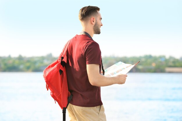 Beau jeune touriste avec carte debout sur la rive du fleuve