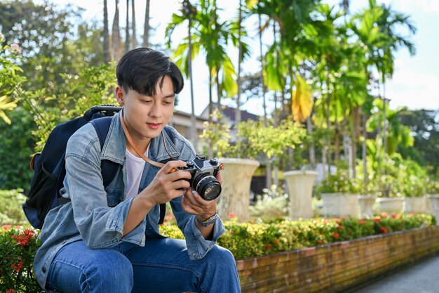 Beau jeune voyageur asiatique se reposant sur un banc vérifiant des photos dans son appareil photo