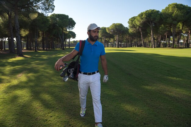 beau joueur de golf du moyen-orient transportant et sac et marchant sur le parcours le beau lever du soleil du matin