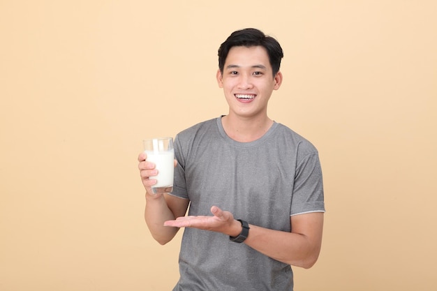 Beau et joyeux jeune homme sportif asiatique tenir un verre de lait frais isolé sur fond