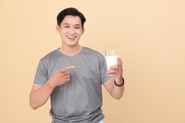 Beau et joyeux jeune homme sportif asiatique tenir un verre de lait frais isolé sur fond