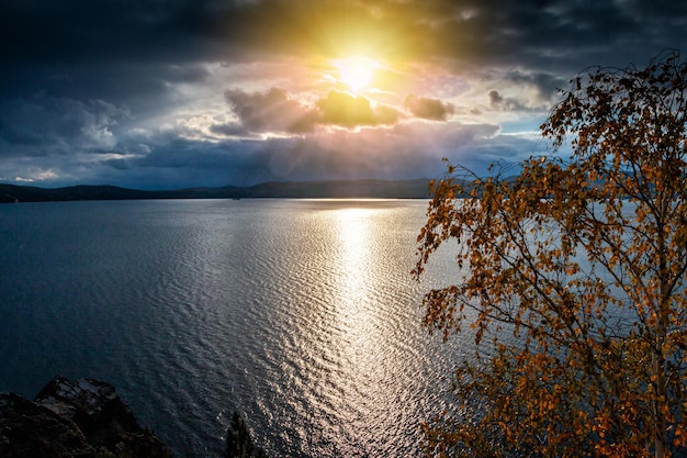 Beau lac et rivage rocheux dans les rayons du soleil du soir de l'automne doré par temps nuageux