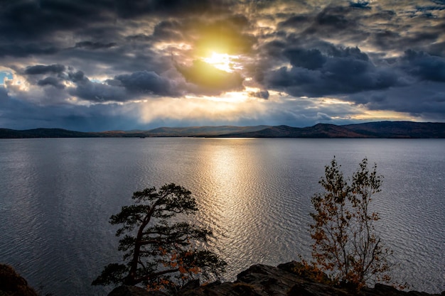Beau lac et rivage rocheux dans les rayons du soleil du soir de l'automne doré par temps nuageux