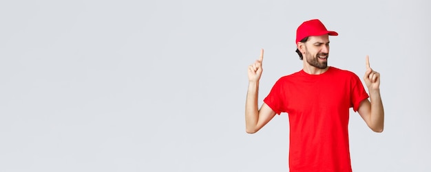 Beau livreur barbu optimiste qui dépense une pause relaxante employé en casquette et t-shirt uniformes rouges