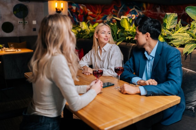 Beau mâle barbu en costume et deux jolies femmes blondes assises au restaurant parlant souriant faisant des toasts s'amusant à célébrer l'anniversaire