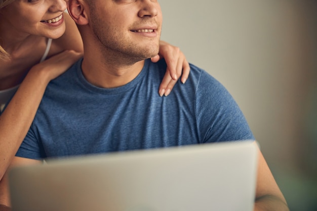 Beau mâle travaillant en ligne sur ordinateur tandis qu'une femme mignonne l'étreint et souriant