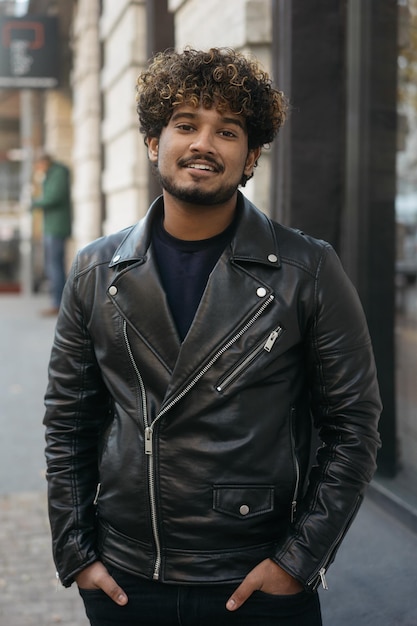 Photo beau mannequin indien souriant portant une veste en cuir noire posant pour une photo dans la rue