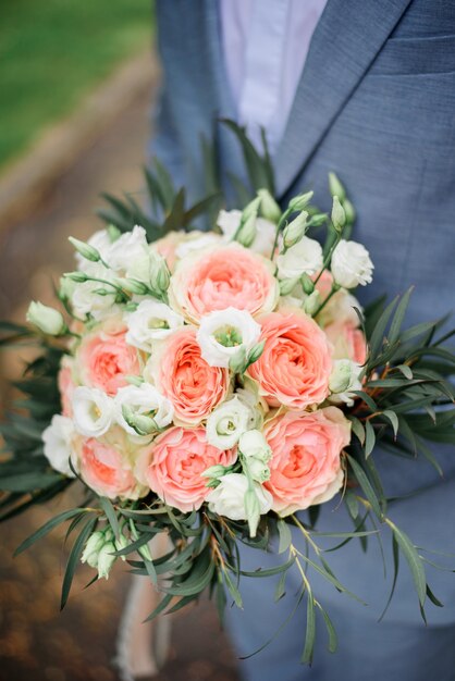 Beau marié en costume gris se dresse avec bouquet rose dans le parc