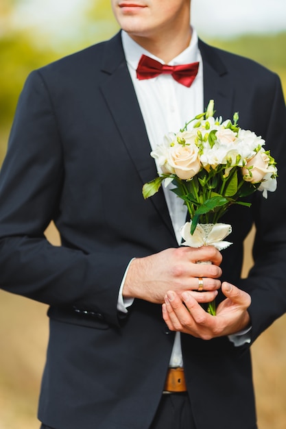 Beau marié fort dans un costume avec une cravate, tenant un bouquet de mariée