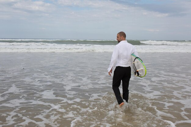 Beau marié surfant à la plage en été