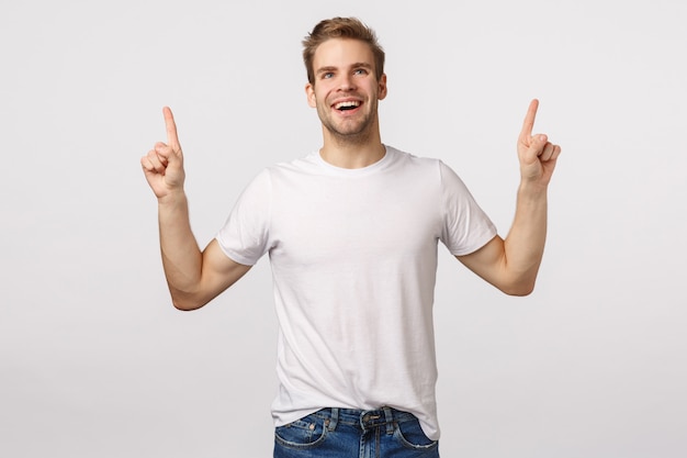 Beau mec blond aux yeux bleus et T-shirt blanc pointant vers le haut