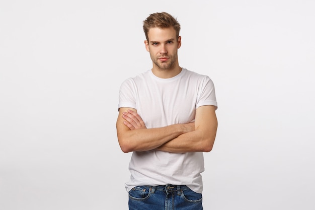 Beau mec blond aux yeux bleus et T-shirt blanc posant avec les bras croisés