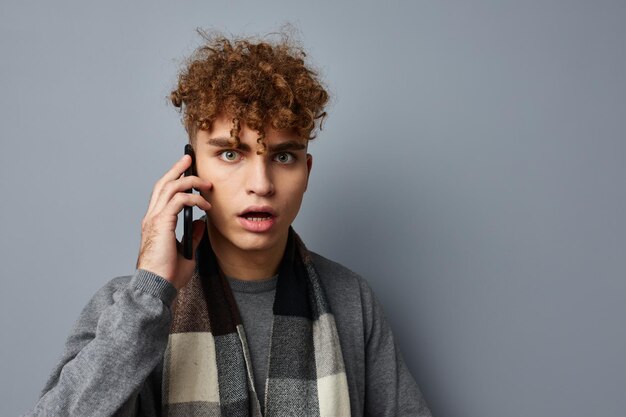 Beau mec dans une écharpe à carreaux parlant au téléphone posant des émotions fond clair