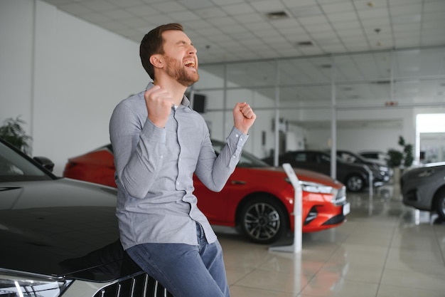 Beau mec émotionnel levant la main et souriant à la caméra Homme riche achetant une voiture au salon de la concession de luxe