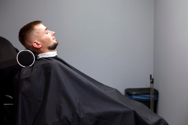 Beau mec est assis dans un salon de coiffure et fait une courte coupe de cheveux à un client