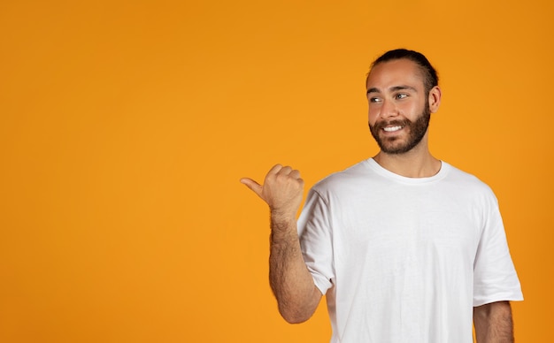 Beau mec européen adulte souriant avec barbe en t-shirt blanc pointe du doigt l'espace libre