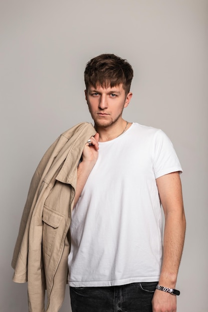Beau mec glamour avec une coiffure dans une veste beige à la mode et un T-shirt blanc pose en studio et regarde la caméra
