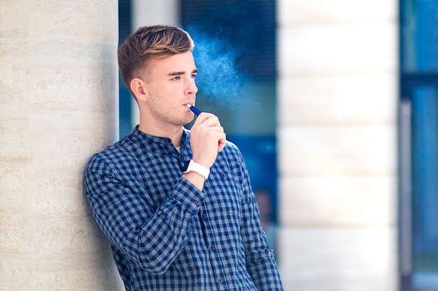 Beau mec, un jeune homme fume, chauffe un produit du tabac, Garçon avec une nouvelle e-ciggarette. Alternative au tabagisme.