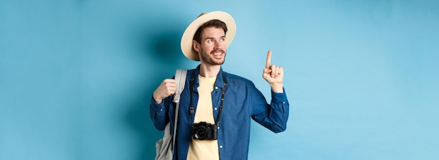 Beau Mec Positif En Vacances Portant Un Chapeau D'été Regardant Et Pointant Vers Le Logo Souriant Heureux