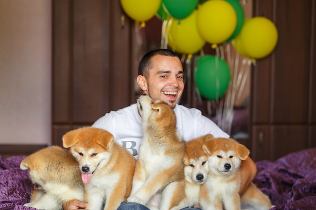 Beau mec s'amuse dans ses bras et joue avec des chiots akita inu