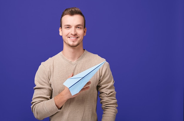 beau mec avec sourire détient avion en papier.