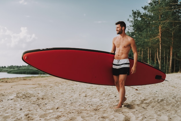 Beau mec sportif avec Surf debout sur la plage.