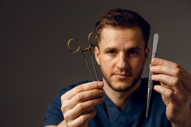 Beau médecin avec des ciseaux chirurgicaux et un porte-aiguille. Homme confiant tenant du matériel médical dans les mains.