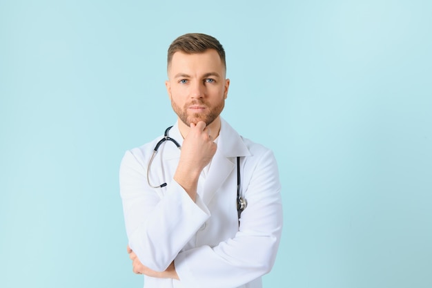 Beau médecin homme portant manteau et stéthoscope sur fond bleu isolé