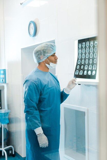 un beau médecin en uniforme et un masque médical tenant des rayons X dans la clinique