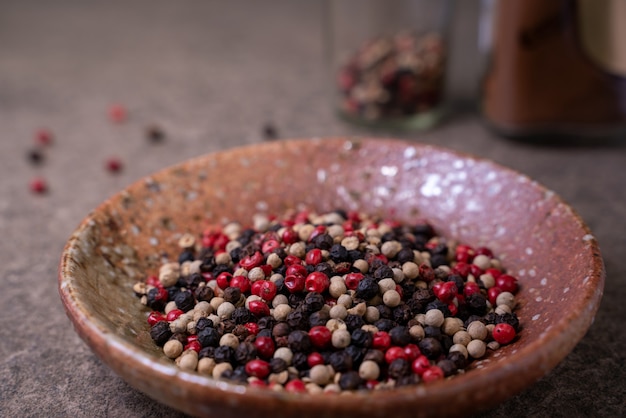 Le beau mélange d'épices est composé de grains de poivre noir, rouge, vert et blanc dans un petit bol sur une table rustique