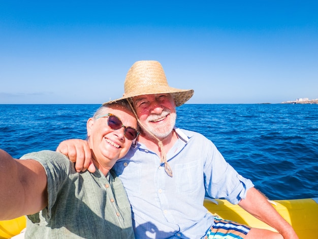 Beau et mignon couple de seniors ou de personnes âgées au milieu de la mer conduisant et découvrant de nouveaux endroits avec un petit bateau. Femme mature tenant un téléphone et prenant un selfie avec son mari