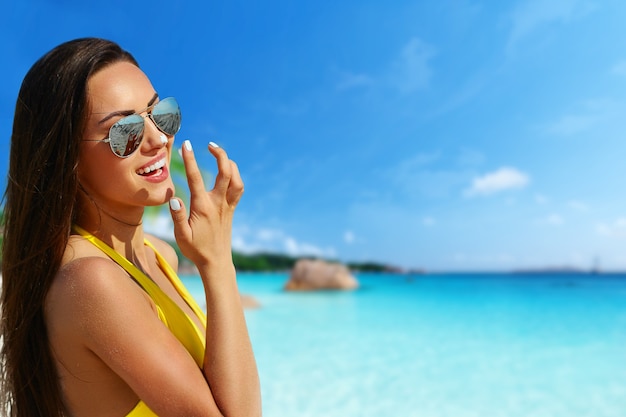 Beau modèle de bikini souriant à la plage tropicale avec fond d'océan