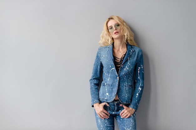 Beau modèle blonde élégante en costume de jeans qui pose en studio