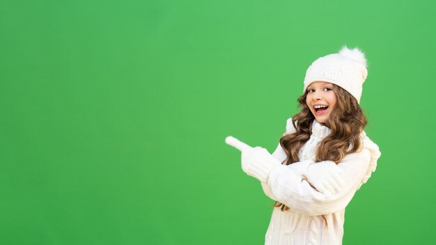 Un beau modèle dans un chandail tricoté chaud pointe la publicité et sourit. modèle de bébé dans des vêtements d'hiver chauds sur fond vert isolé avec espace de copie.