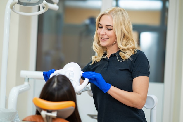 Beau modèle féminin blanchissant les dents dans une clinique dentaire avec un équipement professionnel.