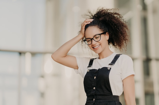 Beau modèle féminin de peau foncée avec des cheveux croquants, baisse les yeux, vêtu d'un t-shirt décontracté blanc