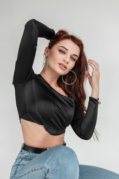 Beau modèle de fille avec un t-shirt noir fashion et un jean bleu vintage pose en studio et regarde la caméra