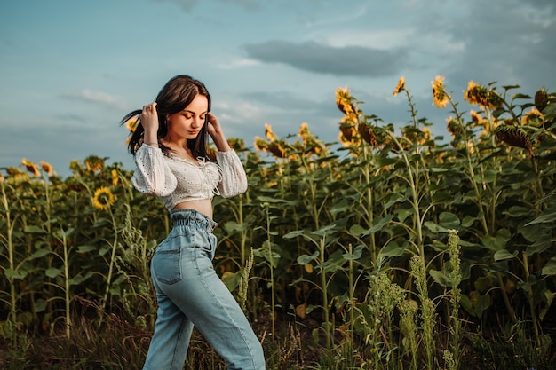 Beau modèle de jeune fille se promène dans un champ de tournesols en fleurs bouquet jaune à l'extérieur du coucher du soleil