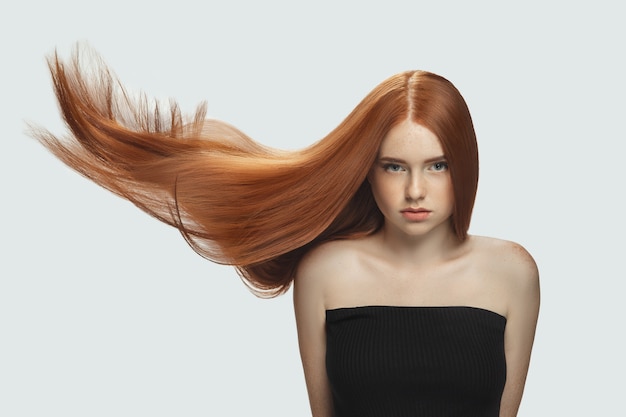 Beau modèle avec de longs cheveux roux lisses et volants isolés sur fond de studio blanc.