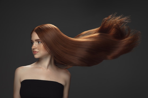 Beau modèle avec de longs cheveux roux lisses et volants isolés sur fond de studio sombre.