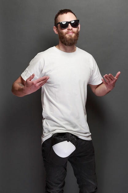 Beau modèle masculin hipster avec barbe portant un t-shirt blanc et une casquette de baseball avec un espace pour votre logo ou votre design dans un style urbain décontracté