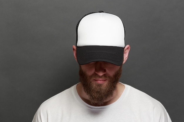 Beau modèle masculin hipster avec barbe portant un t-shirt blanc et une casquette de baseball avec un espace pour votre logo ou votre design dans un style urbain décontracté