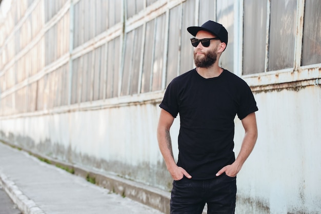 Beau modèle masculin hipster avec barbe portant un t-shirt blanc noir avec un espace pour votre logo ou design dans un style urbain décontracté