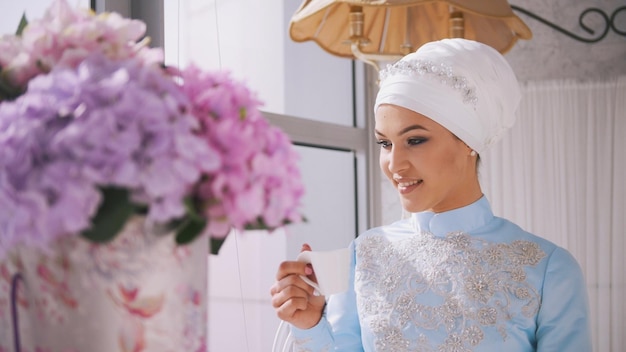 Beau modèle musulman en robe de mariée bleue buvant du café