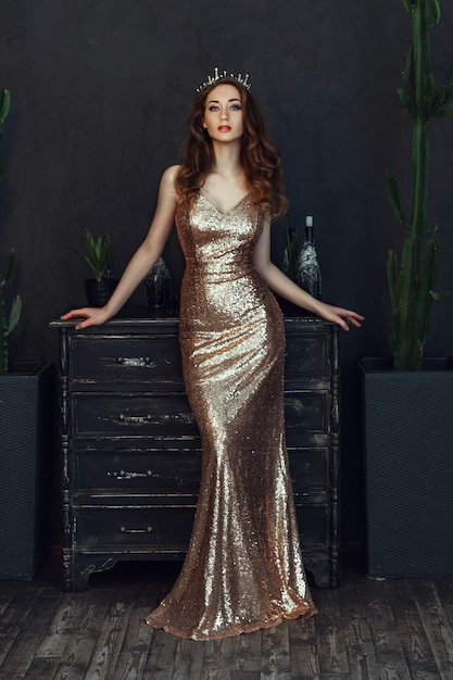 Beau modèle portant une robe dorée pose dans une pièce sombre